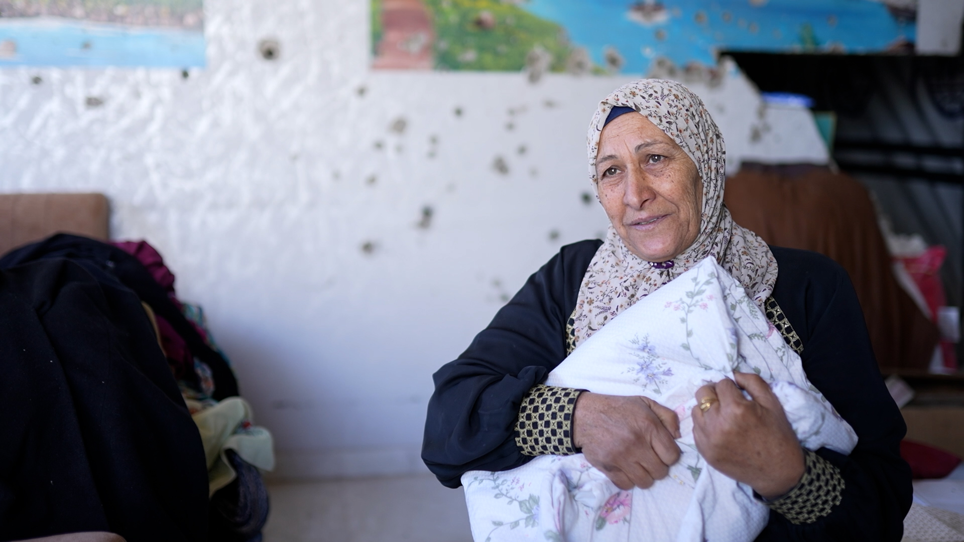 woman holding folded comforter in front of wall with bullet holes